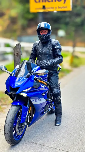 Standing beside the bike by the roadside, helmet on, with trees behind